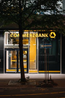 Gece bir ağacın arkasındaki Commerzbank şubesinin dikey görüntüsü.