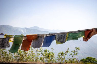 Gökyüzünde asılı renkli dua bayrakları ve arka planda dağlarla yakın çekim.