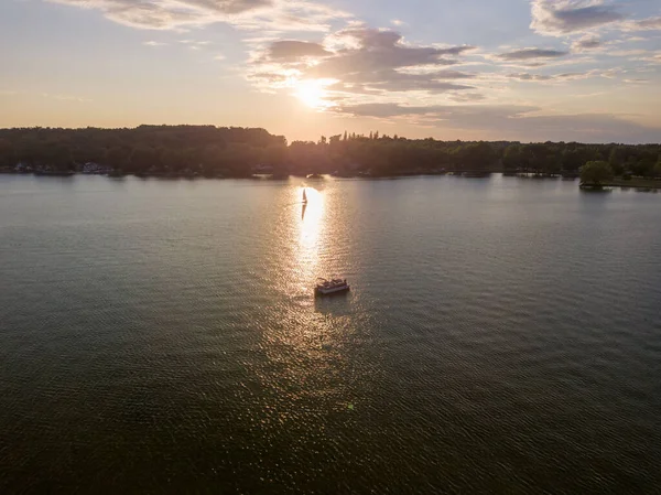 A bird\'s eye view of a boat sailing in the Owasco lake against green shore in New York at sunset