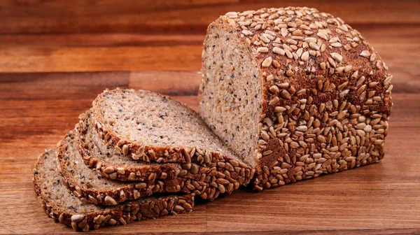 A closeup of sliced loaf of bread with sunflower seeds on the wooden surface.