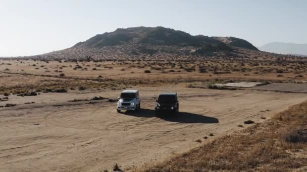天気の良い日に砂漠の道路上の黒と白の車の空中ショット — ストック動画