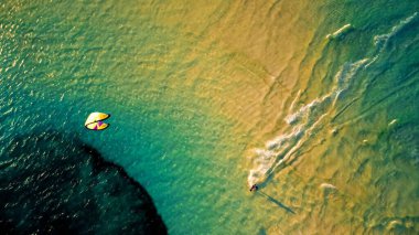 An aerial drone shot of a kite surfer surfing on the calm waters of the ocean