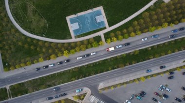 An aerial top view of a basketball court in a green field near an asphalt road busy with traffic