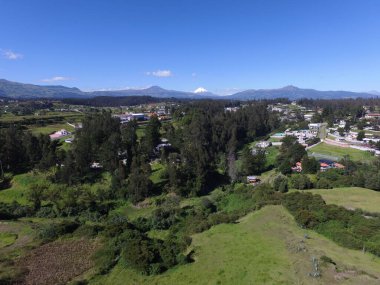 Güneşli bir günde yeşil ormanlarla kaplı tepelerin ve kırsal alandaki evlerin kuş bakışı görüntüsü