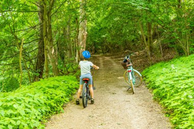 Bisikletli bir çocuk başka bir bisikletin yanında ormanda bir patikada