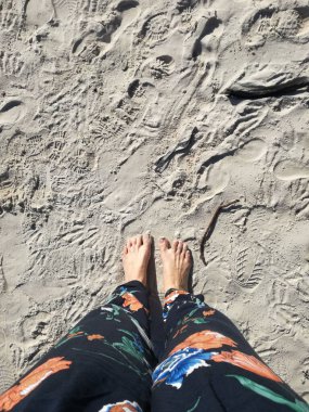 A vertical high angle shot of the woman's feet on the sandy beach.