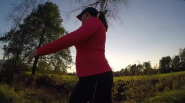 A Caucasian woman in sweat suit and cap having a morning walk at a park with the sun rising in the horizon