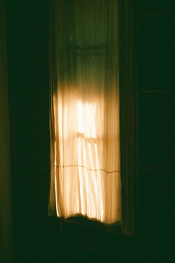 A view of a curtain in a dark room with sunlight