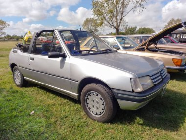 Old silver gray sporty Peugeot 205 two door convertible 1985 - 1992 in the countryside. Nature, grass, trees. Classic car show. Copyspace.