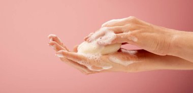 Parlak pembe arka planda sabun ve köpüklü ellerin yakın plan çekimi.