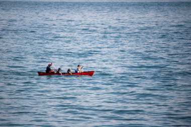The view of the red boat with people floating on the blue sea surface.