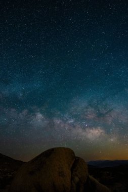A vertical shot of big rock on background of the blissful Milky Way in the sky