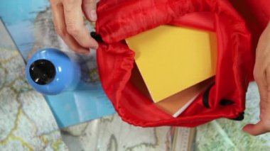 Close red bag full of books , opened maps and water bottle ,