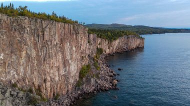 A scenic view of rocky cliffs covered with greenery against a blue sea reflecting the cloudy sky