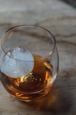 glass dram of whiskey whisky with sphere ice on wood table, barrel