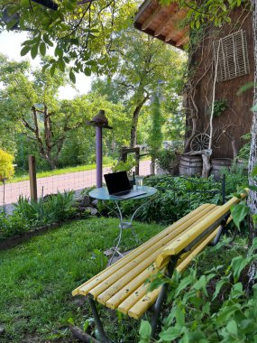 A vertical shot of a bench with a working table with a laptop in the yard.