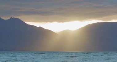 The sun rays pierce the clouds onto a wintery Lake Wakatipu in Queenstown, New Zealand.
