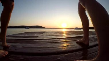 A couple jumping into the sea from a pier while holding hands on the sunset background