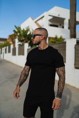 Aynı tişörtü ve şortu giyen dövmeli genç bir adamın dikey fotoğrafı.