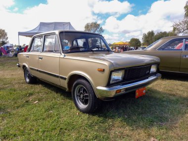 Old beige Fiat 125 Mirafiori four door sedan 1980 in the countryside. Sunny day. Nature, grass, trees. Classic car show.