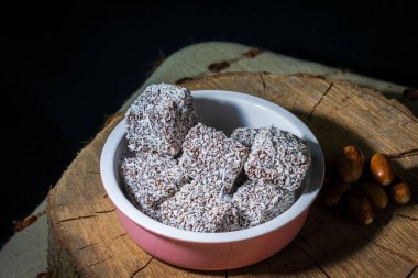 A closeup shot of lamington pies in a pink bowl with hazelnuts on a wooden surface