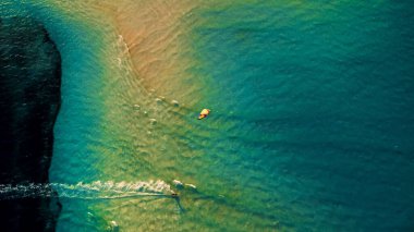 An aerial drone shot of a kite surfer surfing alone on the ocean waters at sunset