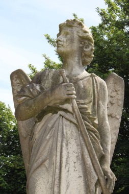 An old ancient sculpture of an angel in a green park
