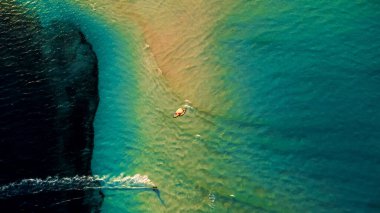 Okyanusun sığ turkuaz suyunun ve bir uçurtma sörfçüsünün hava aracı görüntüsü.