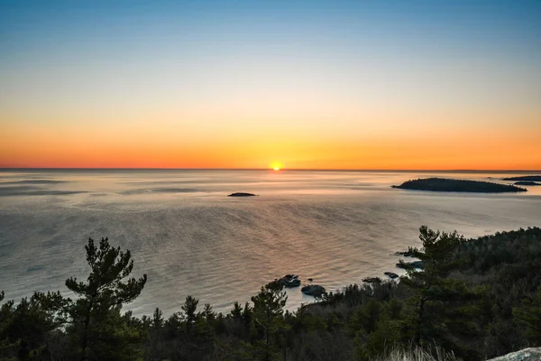 The sun rises over a sleepy Lake Superior.  The rich colors of the sun blend together on the horizan as it meet the deep blues of the lake.