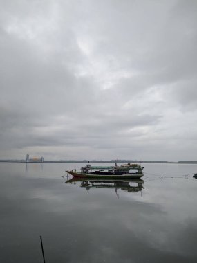 Bulutlu gökyüzünün altındaki sakin bir göldeki balıkçı teknesinin gri pulu.