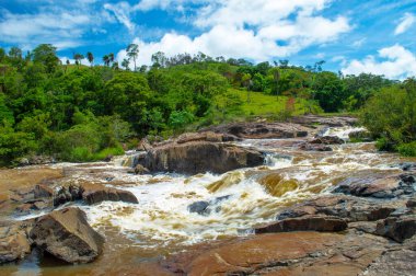 Bulutlu mavi gökyüzü. Çiftlikteki orman. Kayalara düşen şelale..