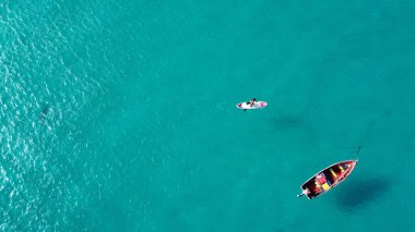 Sörfçülerin hava manzarası ve güneşli bir günde mavi deniz manzaralı bir tekne.