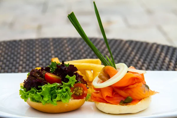 A beautiful shot of a salmon burger, lettuce and tomato burger and fries on a white plate