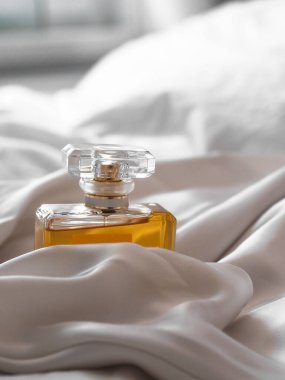 Bulanık bir arkaplanda beyaz bir bez arasında lüks bir kadın parfüm şişesinin dikey çekimi..