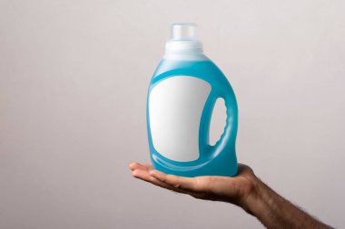Beyaz bir duvara karşı boş etiketli sıvı deterjan şişesini tutan bir adam.