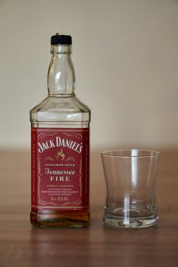 Jack Daniels Tennessee ateş tarçın aromalı viski şişesi yakın çekim, ahşap bir masa üzerinde boş bir bardak ve bulanık bir arka plan