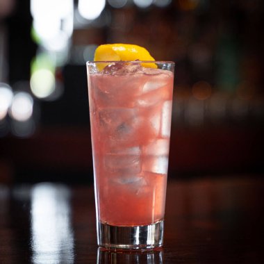 Kırmızı bir kokteylin dikey yakın çekimi. Barda mango dilimi ve buz küpleri var.