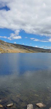 Güneşli bir baharda sakin göl üzerinde bulutlu mavi gökyüzünün dikey görüntüsü.