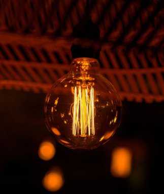 Karanlık bir odada ahşap bir tavandan sarkan bir ampulün yakın çekimi güzel görünüyor.