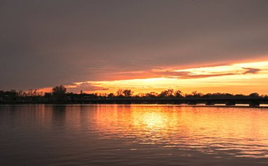 Sakin bir göle yansıyan manzaralı bir gün batımı.