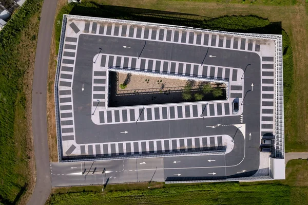 Aerial top down view with a single car parked in graphic outline parking lot with arrows and spots marked in the dark asphalt on elevated roof top.