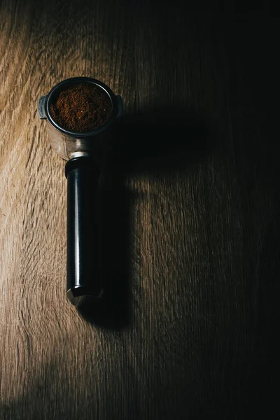 A vertical shot of a coffee portafilter with coffee in it on a wooden table