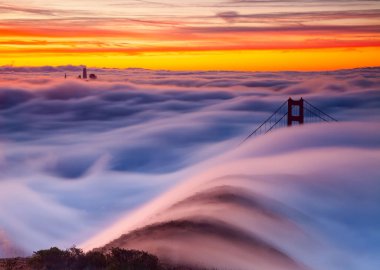 Puslu bir günde altın kapı köprüsünün nefes kesici bir görüntüsü. Arka planda güzel bir turuncu gün batımı var.