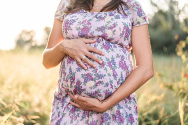 Bulanık bir geçmişi olan, çiçekli bir elbiseyle karnını tutan hamile bir kadının sığ odağı.