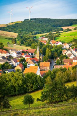 Almanya 'nın Niederkirchen yakınlarında ağaçlar ve çayırlarla çevrili küçük bir kasabanın manzaralı bir görüntüsü.