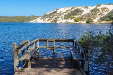 Sakin bir gölün üzerindeki ahşap bir rıhtımın doğal görüntüsü ve berrak gökyüzü.