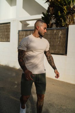 Bej tişörtlü ve yeşil şortlu genç bir adamın sokakta yürürken çekilmiş dikey bir fotoğrafı.