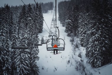 A young male on a ropeway passing through snowy pine tree forest in the French Alps