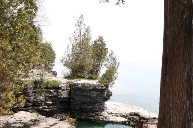 A calm lake with a rocky coast and trees under the clear sky