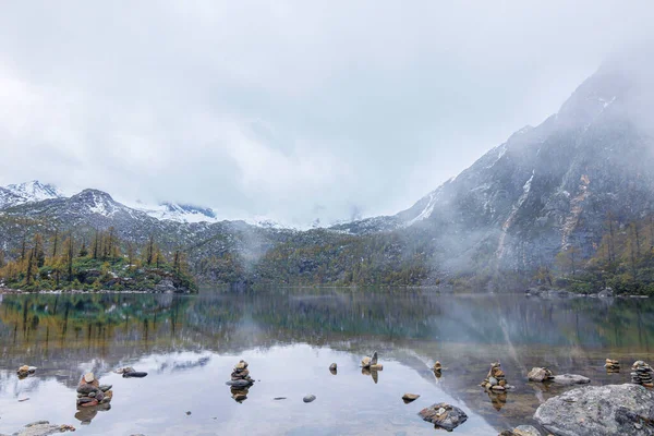 A tranquil scenery of snowy mountains reflecting on the lake during a cloudy weather